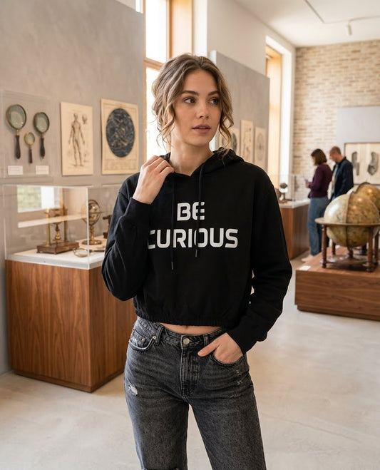 Model wearing a black BE CURIOUS cropped hoodie with high-waisted grey jeans.